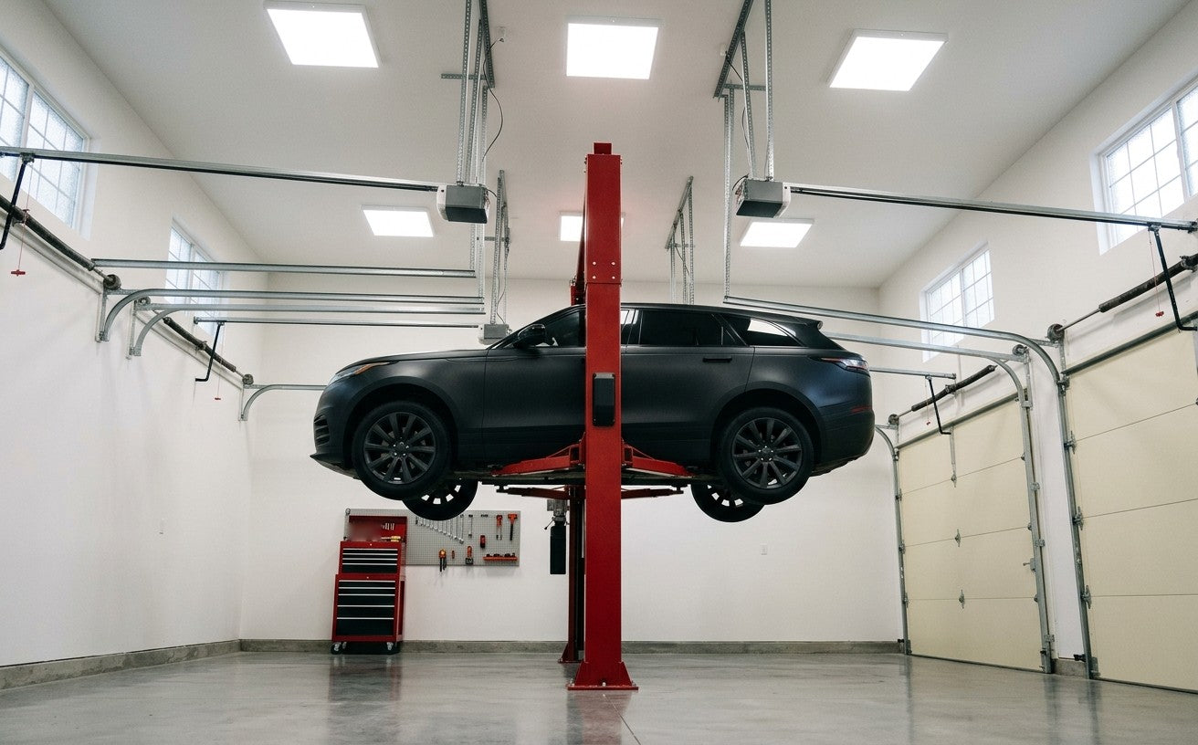 Black SUV raised high on a red two-post lift in a tall garage with high ceilings