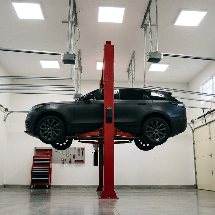 Black SUV raised high on a red two-post lift in a tall garage with high ceilings