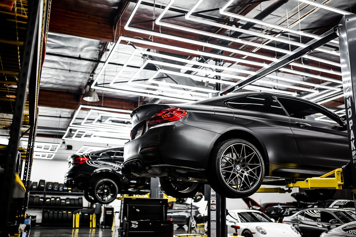 Matte black sports coupe raised on a two-post car lift in a modern shop